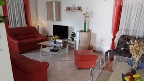 A living room with red sofas, a glass coffee table, a TV, and a dining area with a table and chairs. - Holiday apartment with barbecue facilities and terrace (Vir)