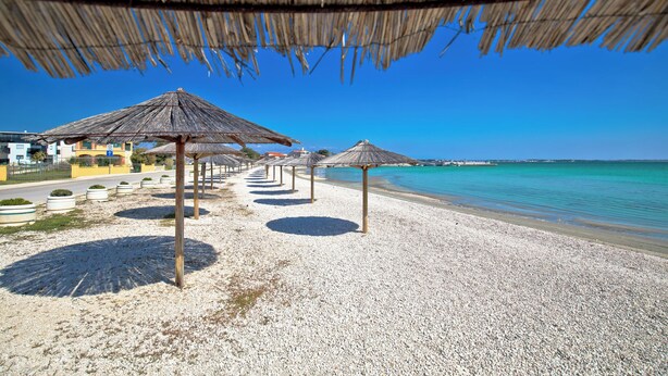 A beach with thatched umbrellas and pebbled beach. - Holiday apartment with barbecue facilities and terrace (Vir)