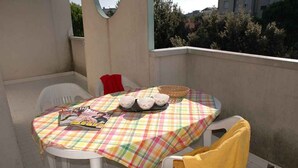 Un balcone con un tavolo apparecchiato per il tè, caratterizzato da una tovaglia a quadri, sedie bianche e un asciugamano giallo.
