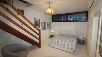 Une chambre avec un escalier en bois, un lit recouvert d’une couverture à carreaux, une table de chevet avec une lampe et une fenêtre avec des rideaux bleus.