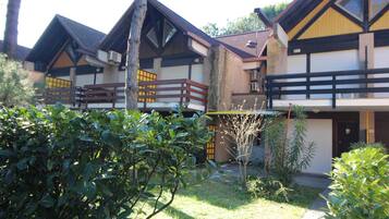 Une rangée de chalets traditionnels en bois, dotés de balcons, et entourés d’une végétation luxuriante et bien entretenue.