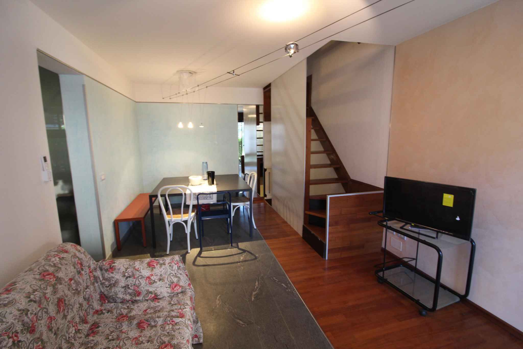 Un espace de vie compact comprenant un canapé, une table à manger avec des chaises, un téléviseur posé sur un meuble et un escalier menant à un niveau supérieur.