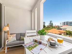 A balcony with a white table, a grey sofa, a potted plant, a newspaper, a cup of coffee, and a glass of orange juice. - Modern South Brisbane Apt w/ Pool & Gym (Brisbane)