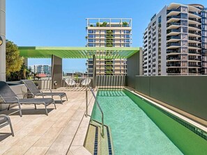 A rooftop pool area with lounge chairs and a pergola, surrounded by high-rise buildings. - Modern South Brisbane Apt w/ Pool & Gym (Brisbane)