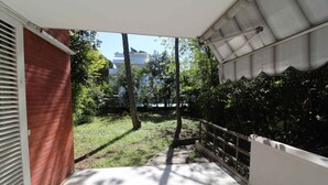 A balcony with a view of a grassy area and trees, a red brick wall, and a white railing. - Holiday apartment mit Terrasse (Lignano Sabbiadoro)