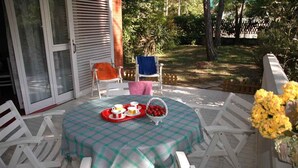An outdoor patio with a table set for a meal, surrounded by white chairs. - Holiday apartment mit Terrasse (Lignano Sabbiadoro)