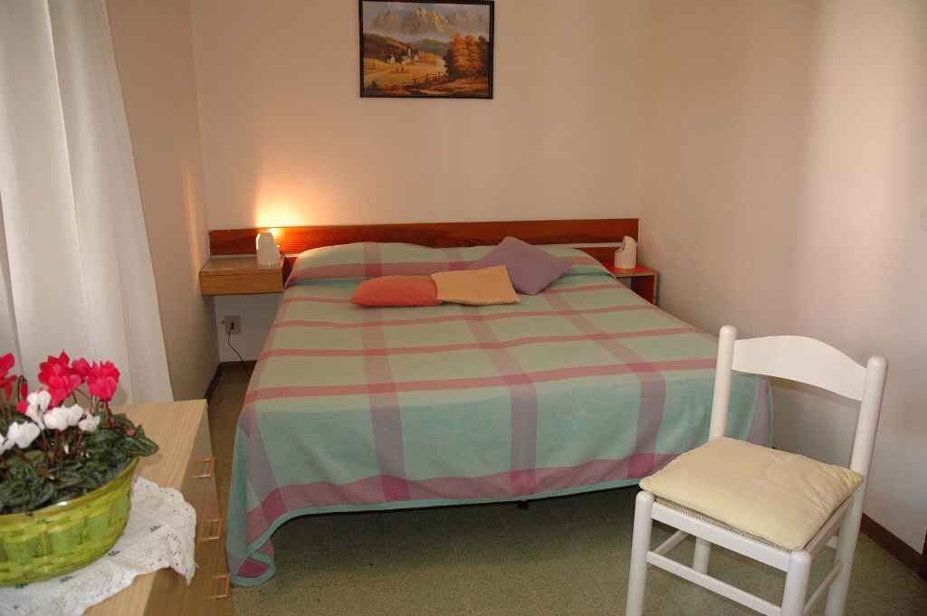 Une chambre à coucher bien rangée, avec un lit, une table de chevet, une lampe et une chaise.