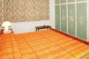 Ein Zimmer mit einem großen Bett, einem kleinen Tisch, einer Lampe und einem grünen Schrank mit Verzierungen.