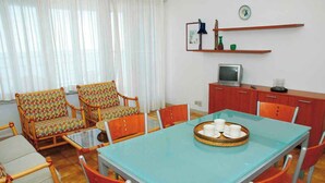 A dining area with a glass table, wicker chairs, and a television on a wooden cabinet. - Holiday apartment mit Meerblick (Lignano Sabbiadoro)