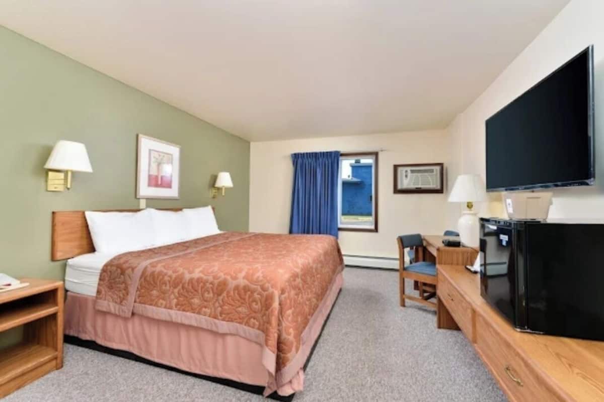 A hotel room with a bed, a desk, a television, and a window with curtains.