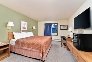A hotel room with a bed, a desk, a television, and a window with curtains.