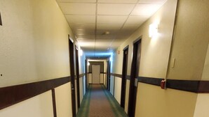 A long, narrow hotel corridor with a patterned carpet, wooden handrails, and doors leading to rooms.