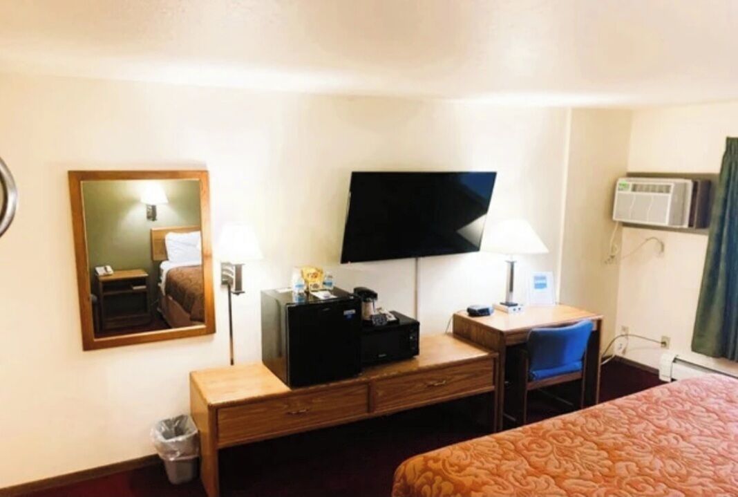 A hotel room with a bed, a desk with a computer, a TV, and a mirror.