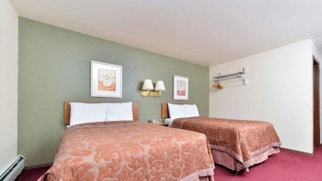 Habitación de hotel con dos camas, una pared verde y obras de arte enmarcadas.