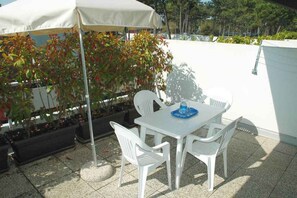 A patio with a white table and chairs, a white umbrella, and potted plants. - Holiday apartment with large corner terrace (Lignano Sabbiadoro)