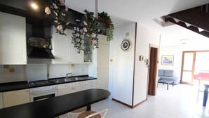 Una cocina con armarios blancos, encimera negra y una zona de comedor con sillas de mimbre.