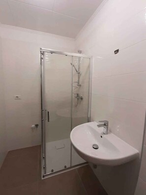 Ein modernes Badezimmer mit Duschkabine aus Glas, einem weißen Waschbecken und gefliesten Wänden.