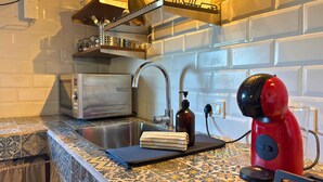 Een keuken met een roestvrijstalen spoelbak, een rode waterkoker, een broodrooster en een decoratieve achterwand.