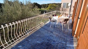 Een terras met een blauwe betegelde vloer, een witte metalen reling, en een tafel met stoelen.