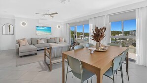 Uma sala de estar moderna com um conjunto de sofá, uma mesa de jantar com cadeiras e uma grande janela com vista para a cidade.