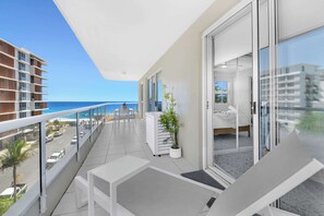 Een balkon met uitzicht op de oceaan, een bed en een bloempot.