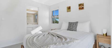 A bedroom with a bed, a nightstand, a ceiling fan, a window, and artwork on the wall.