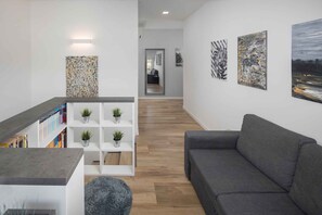 Un salon moderne avec un canapé gris, une étagère blanche agrémentée de plantes et des œuvres d’art accrochées aux murs.