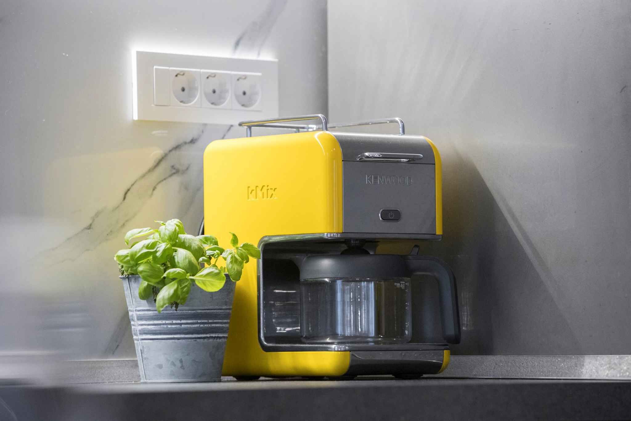 A yellow coffee maker on a kitchen counter with a potted basil plant beside it.