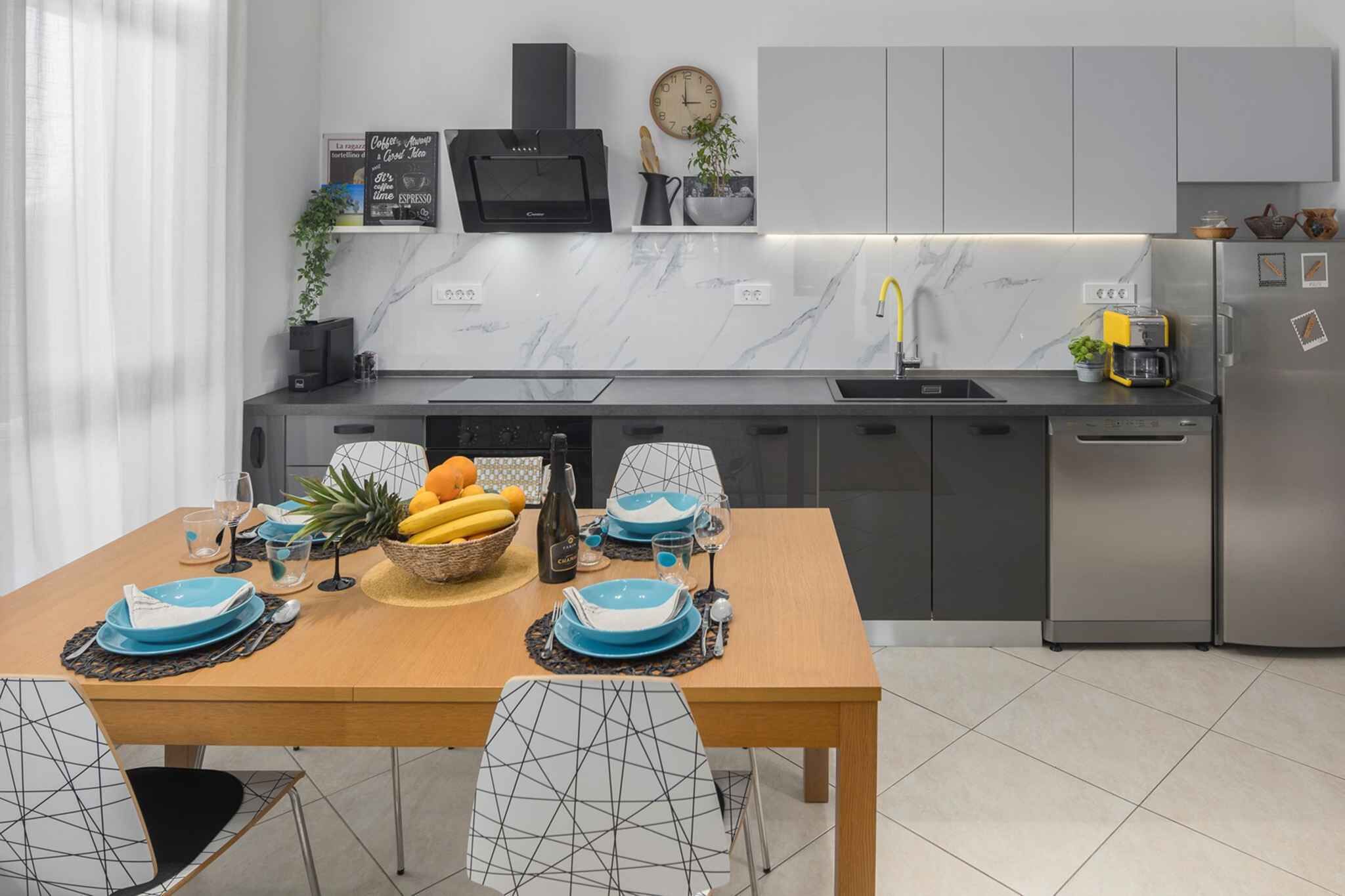 A modern kitchen with a marble countertop, a built-in oven, and a stainless steel refrigerator.