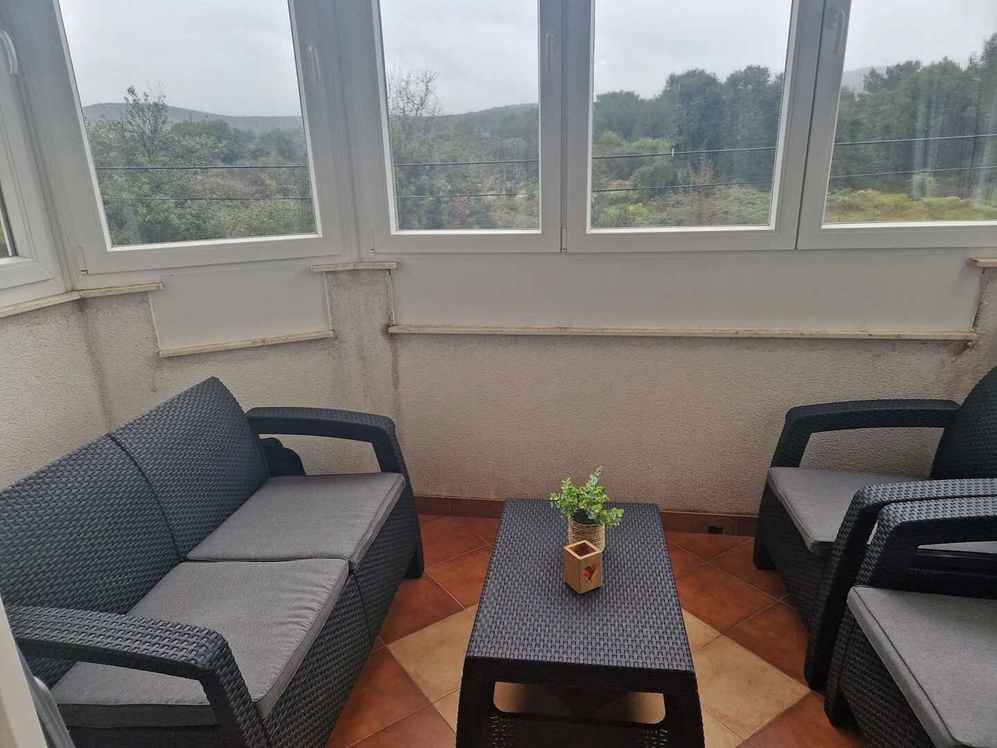 En lille, lukket patio med to grå sofaer og et centralt placeret bord, med en potteplante.