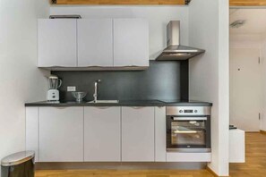 Eine kleine Küche mit weißen Schränken, einer Edelstahl-Dunstabzugshaube, einem eingebauten Backofen und einer Arbeitsplatte mit Toaster und einem Glasbehälter.