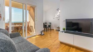 Ett modernt vardagsrum med en stor platt-TV, en soffa och en matplats med bord och stolar.