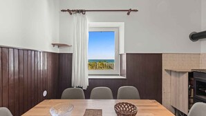 Ein Essbereich mit einem Holztisch, Stühlen, Meerblick und einem Fenster mit Vorhang.