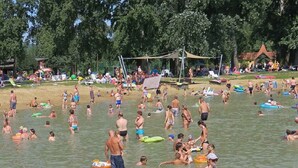 Une plage bondée où l’on voit des gens se baigner et utiliser des bouées gonflables.