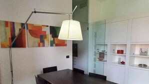 En matplats med ett mörkt träbord och stolar, en modern lampa och en färgstark, abstrakt tavla på väggen.