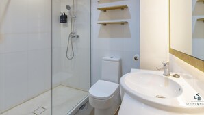 Un baño moderno con ducha de vidrio, inodoro blanco y lavamanos con espejo.