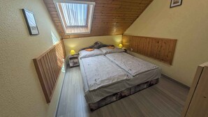 A small, cozy bedroom with a sloped ceiling, a skylight, a bed with a striped bedspread, and two bedside lamps. - Holiday apartment with large terrace, air conditioning and WiFi (Balatonboglár)