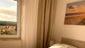 Ein Hotelzimmer mit Bett, Handtüchern, einem Fenster mit Blick auf Gebäude und einem Bild an der Wand.