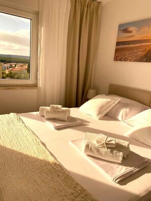 A hotel room with a bed, towels, a window with a view of buildings, and a painting on the wall. - Holiday apartment With sea view and large terrace (Punat)