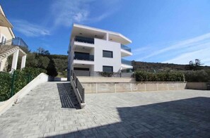 A modern multi-story building with a flat roof, a staircase leading to the entrance, and a paved courtyard. - Holiday apartment With sea view and large terrace (Punat)