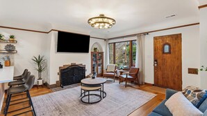 Een ruime woonkamer met een open haard, een ronde salontafel en een grote televisie die aan de muur is bevestigd.