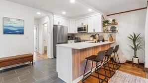 Een moderne keuken met witte kasten, een centraal eiland met barkrukken, roestvrijstalen apparatuur en een houten accentmuur.