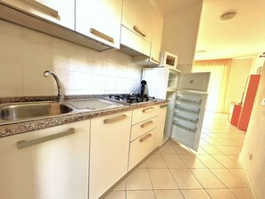 A kitchen with a stainless steel sink, a gas stove, and a built-in refrigerator. - Holiday apartment with garden near the sea (Bibione)
