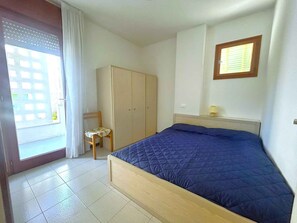 Quarto com cama, guarda-roupa, cadeira e janela.