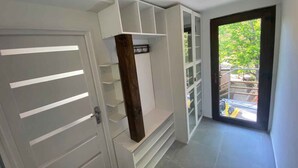 Um interior moderno com estantes embutidas, uma porta com ripas horizontais e vista para o exterior através de uma porta de vidro.