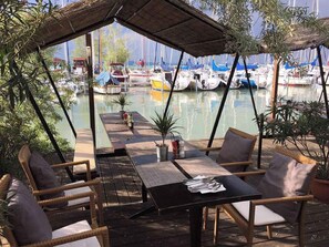 Ein Essbereich im Freien mit Korbmöbeln und einem Tisch, mit Blick auf eine Marina und Boote.