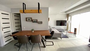 Uma área de jantar moderna com uma mesa de madeira, quatro cadeiras e um sofá ao fundo.