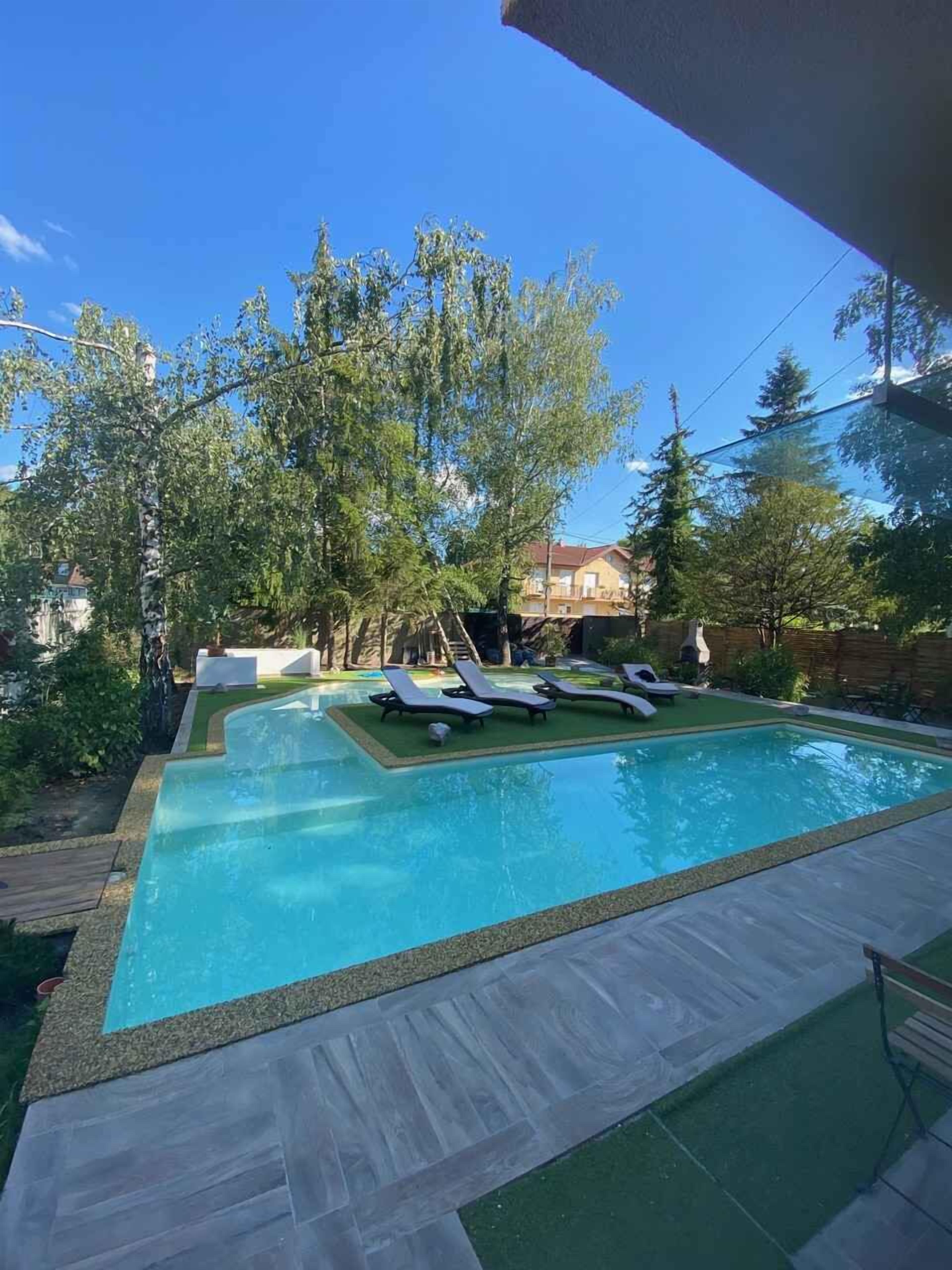 Ein Swimmingpool mit Liegestühlen, umgeben von Bäumen und einem Gebäude im Hintergrund.