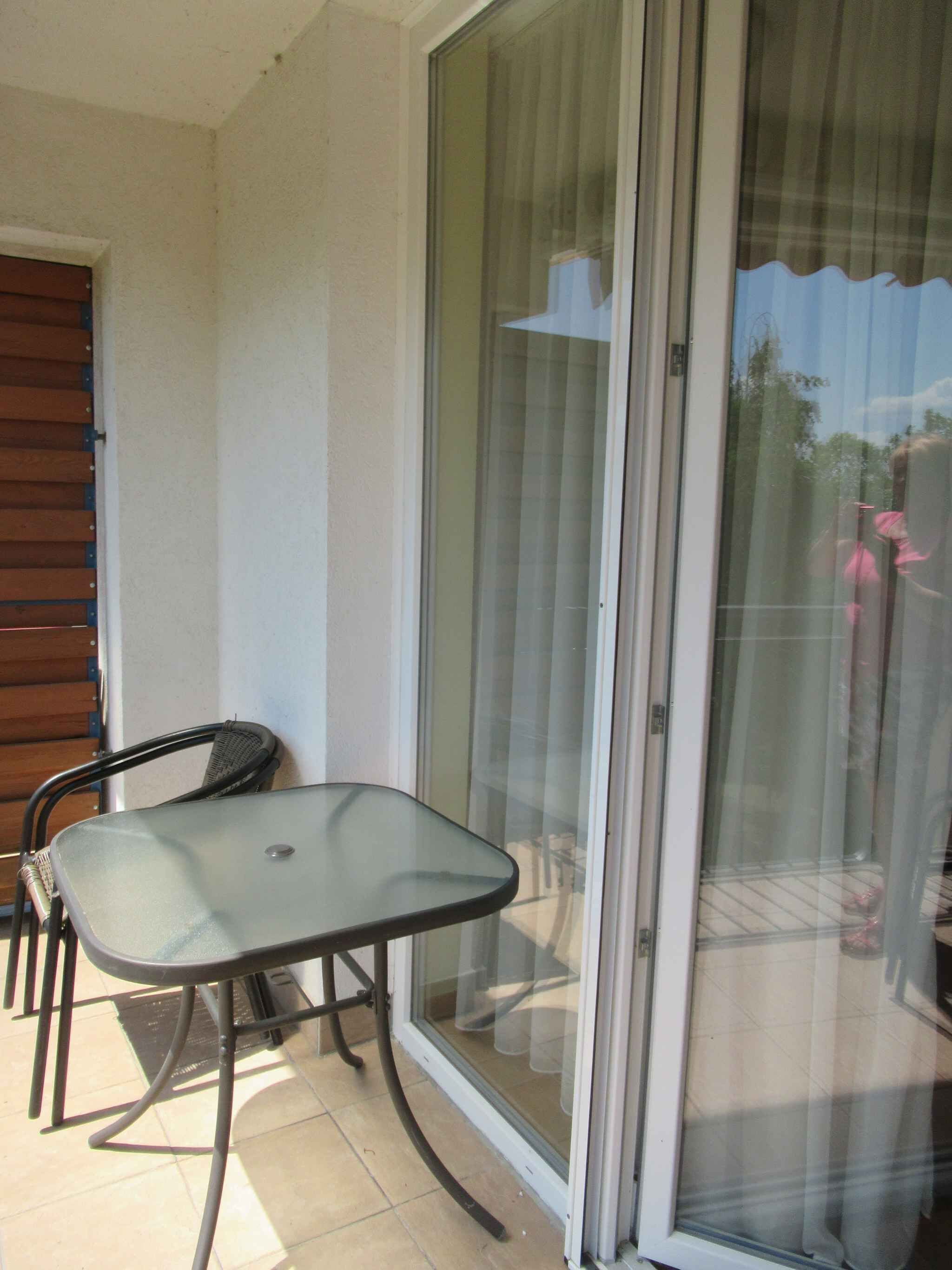 Ein Balkon mit Glastür, einem Metalltisch und zwei Stühlen.