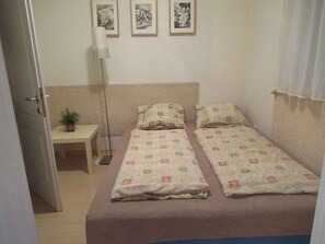 A small, single-bed room with a beige carpet, a bedside table with a plant, and a floor lamp. - Holiday apartment on the Csopak promenade (Csopak)